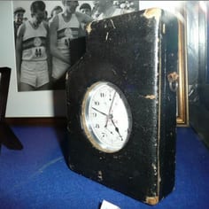 Stop watch used by Bedford Jew, Harold Abrahams (Olympic Gold Medallist, Paris, 1924) used to time the first sub-four minute mile by Roger Bannister. In the back ground is part of a photograph showing the iconic moment at the Iffley Track, Oxford.