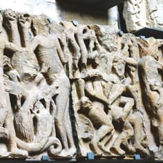 West Front Frieze, map, 1a - Part of the original West Front Frieze, now preserved within the Cathedral, showing the torments of Hell.  Much of the original frieze on the exterior has been restored with exact copies of the decayed originals.  Due to on-going restoration work, some of the panels on the West Front have been covered in protective cases at the time of writing.  The figures in the  central panel may represent Jews being punished for the sin of Avarice.  The hair of the sinners is being pulled in to a shape reminicent of one of the identifiying Jewish hats (the Phrygian hat).